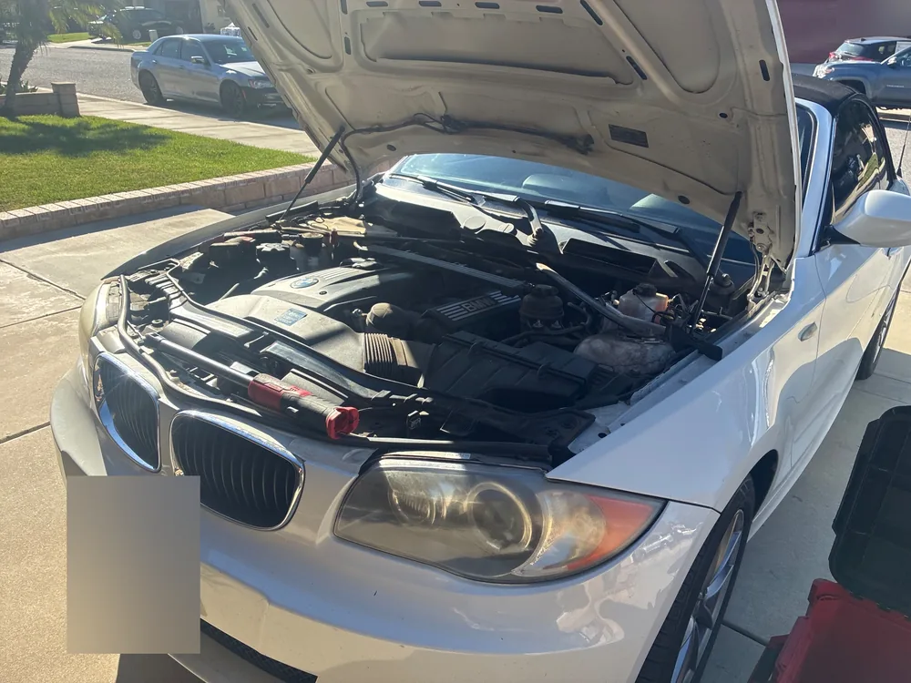 White BMW 128i convertible with the hood up in a driveway and a tech's tools across the front