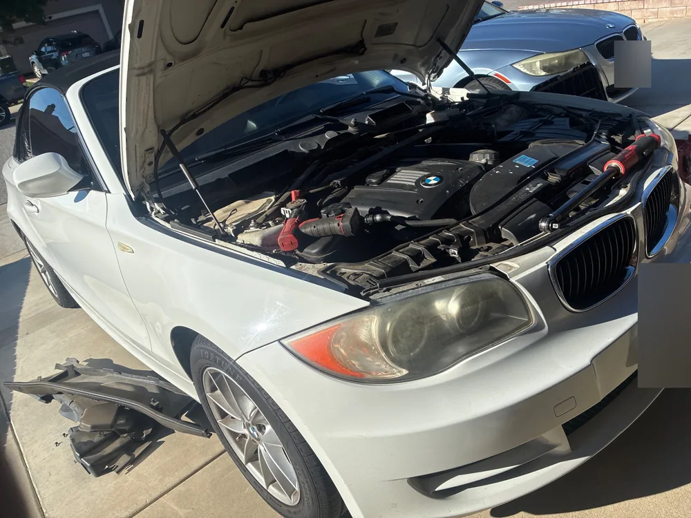 BMW 128i convertible from the front corner with the hood open and tools on the engine