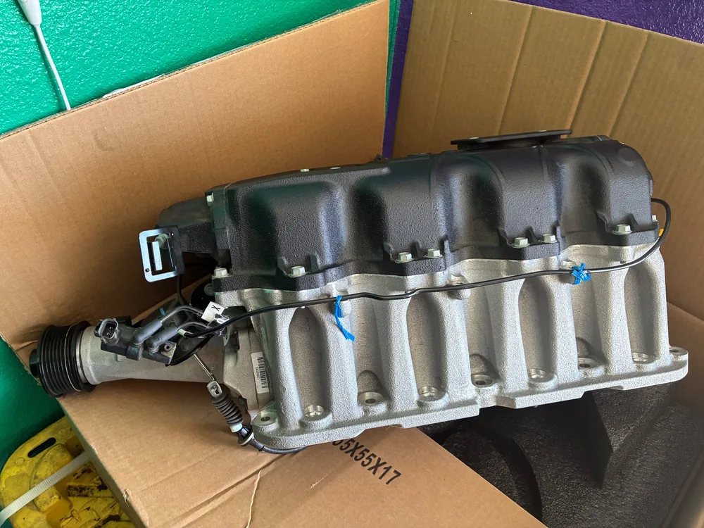 A new supercharger with its intake manifold sitting in a shipping box