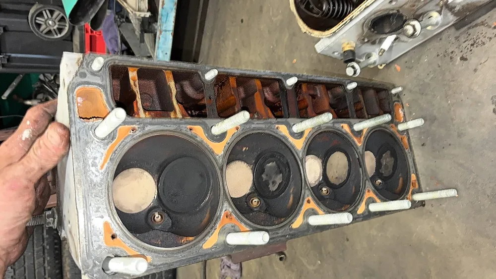 A V8 cylinder head held up on the bench with the head studs still in