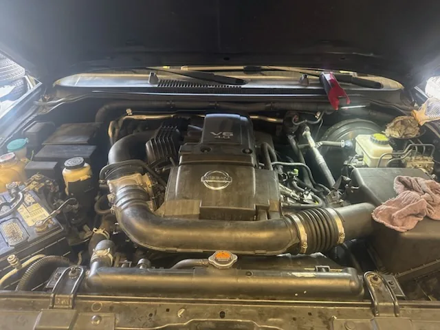 The V6 engine bay of a Nissan Pathfinder with the hood open in the shop