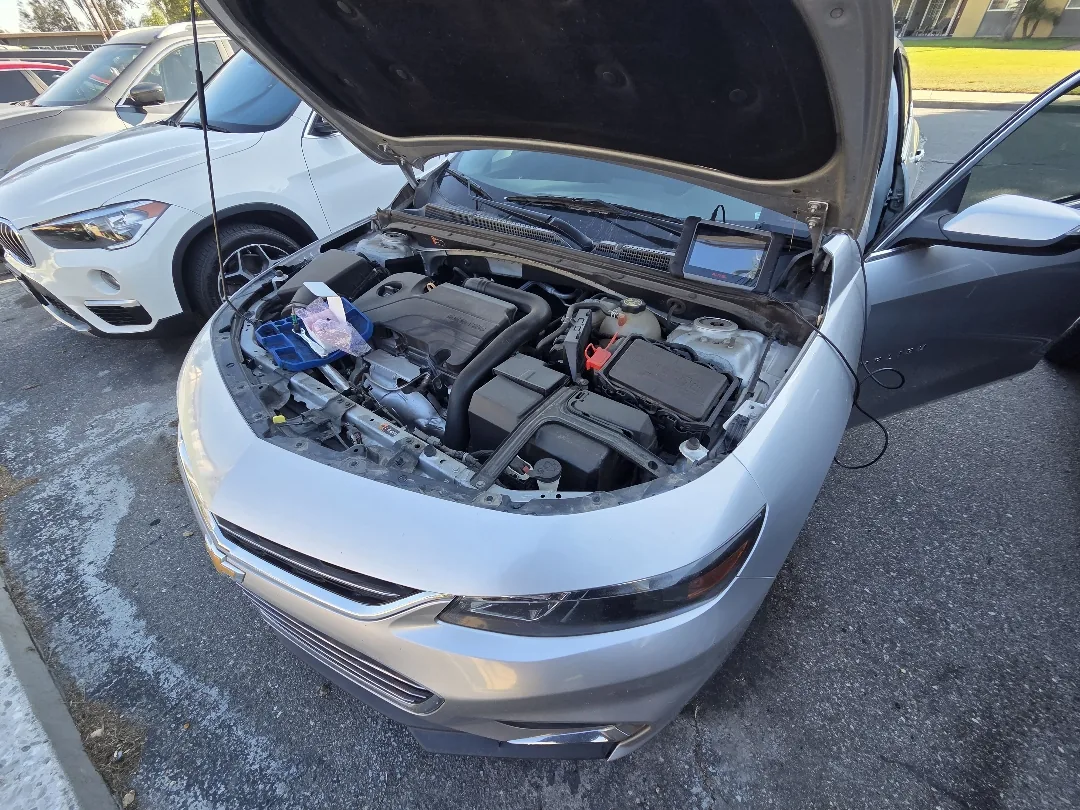 Hood raised on a Chevy sedan during a mobile diagnostic at the curb