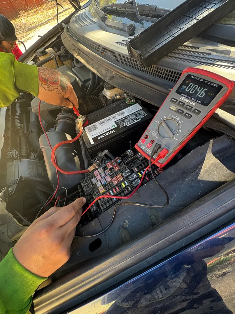 Probing the underhood fuse box with a multimeter to trace an electrical fault