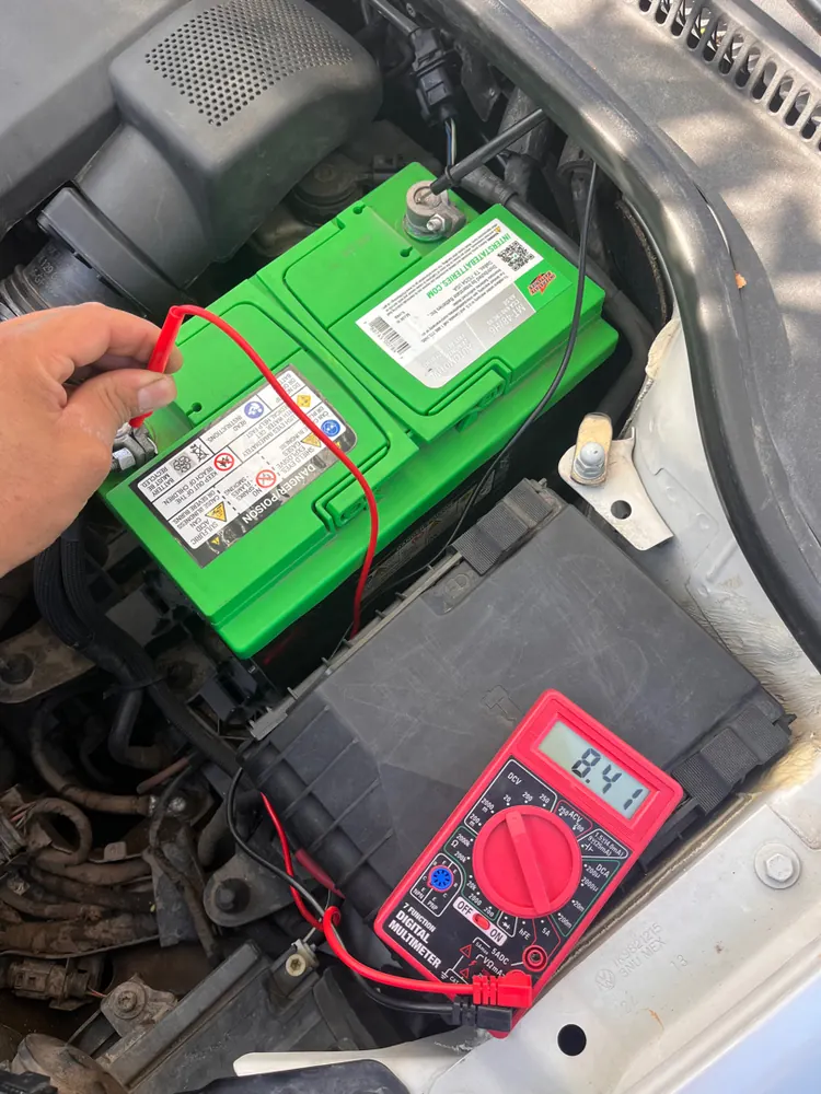 Multimeter connected to a battery checking for electrical draw during diagnosis